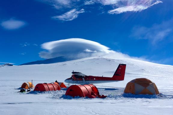 Twin Otter and tents at Mount Sidley Base Camp. Mount Sidley is in the background, with its summit obscured by lenticular clouds.